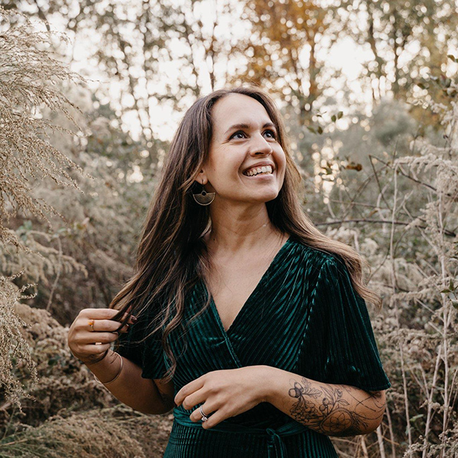 A photograph of Nina standing in a green dress with trees in the background.