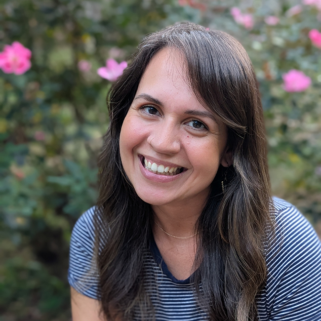 A photograph of Nina standing in a green dress with trees in the background.